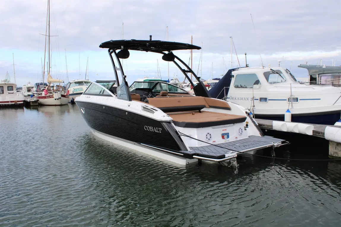 Cobalt boat docked at a marina, surrounded by various boats, with cloudy skies and calm water reflecting the scene.
